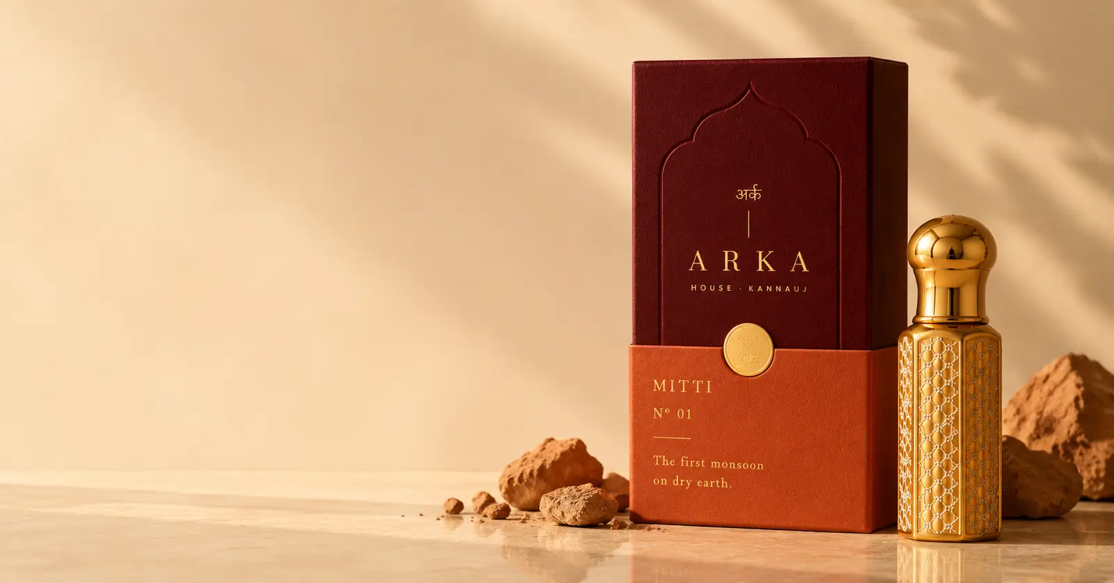 The Mitti box and gold flacon on warm stone with pieces of clay